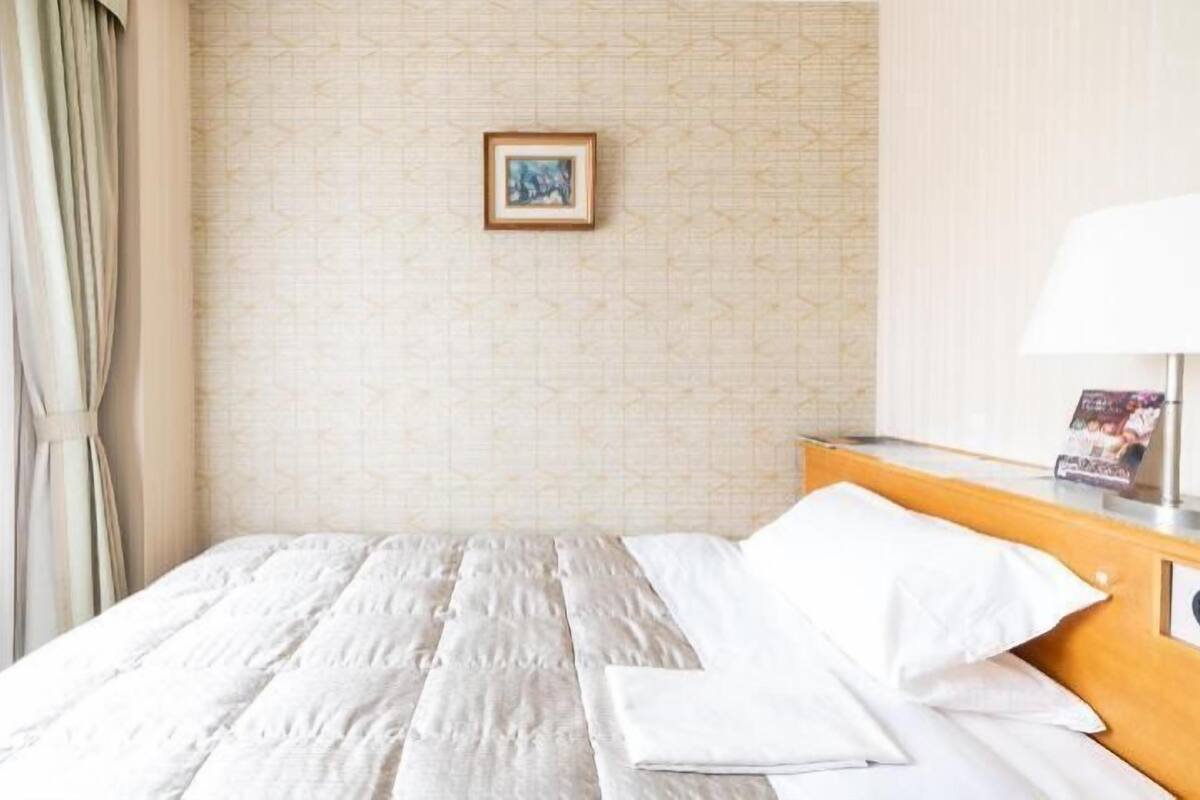A hotel room with a neatly made bed, a framed picture on the wall, and a lamp on the nightstand.