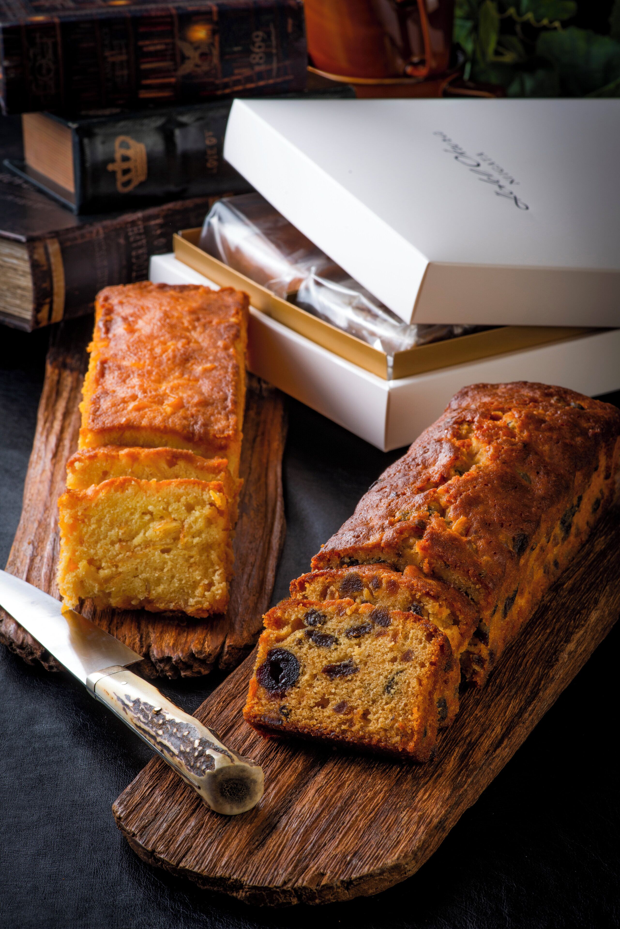 A loaf of bread on a wooden board with a knife, surrounded by books and a white box.