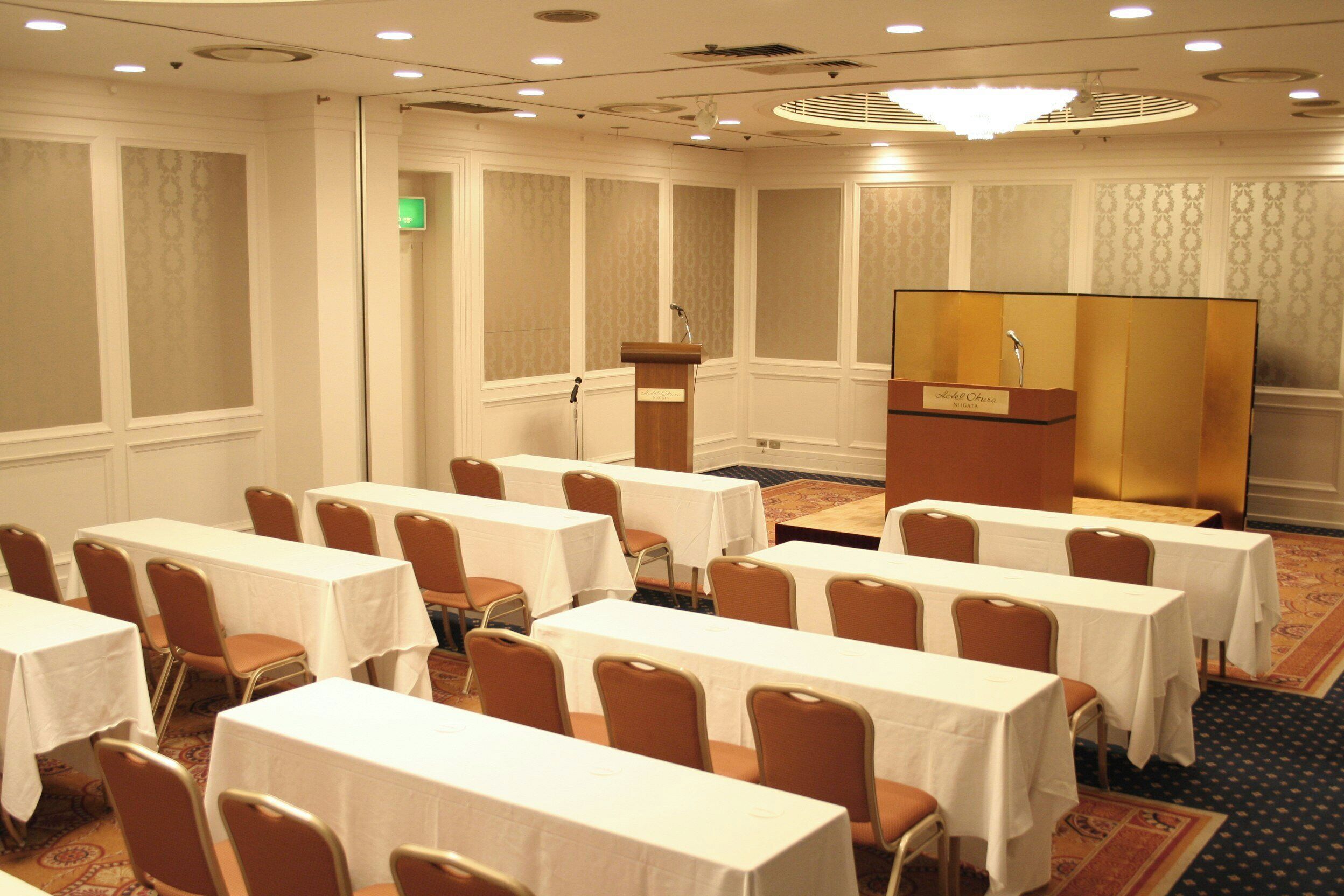 A conference room with tables and chairs, a podium, and a carpeted floor.