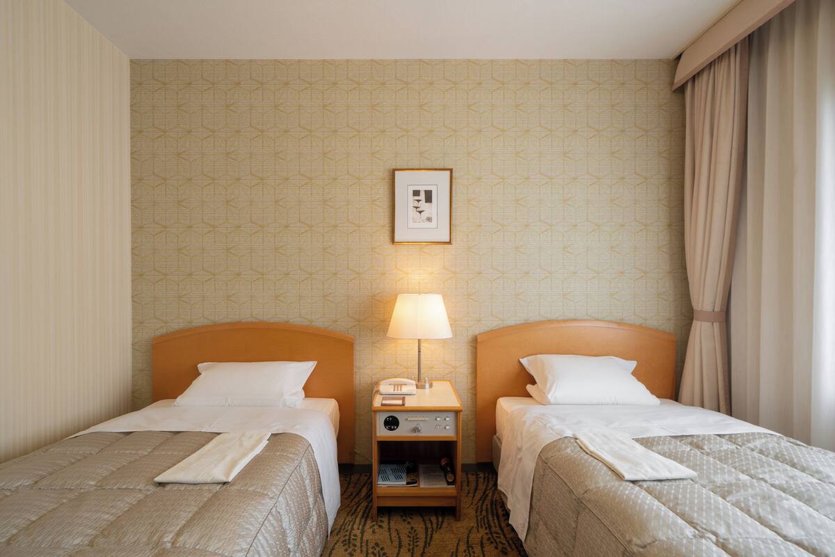 A hotel room with two beds, a nightstand with a lamp, and a framed picture on the wall.