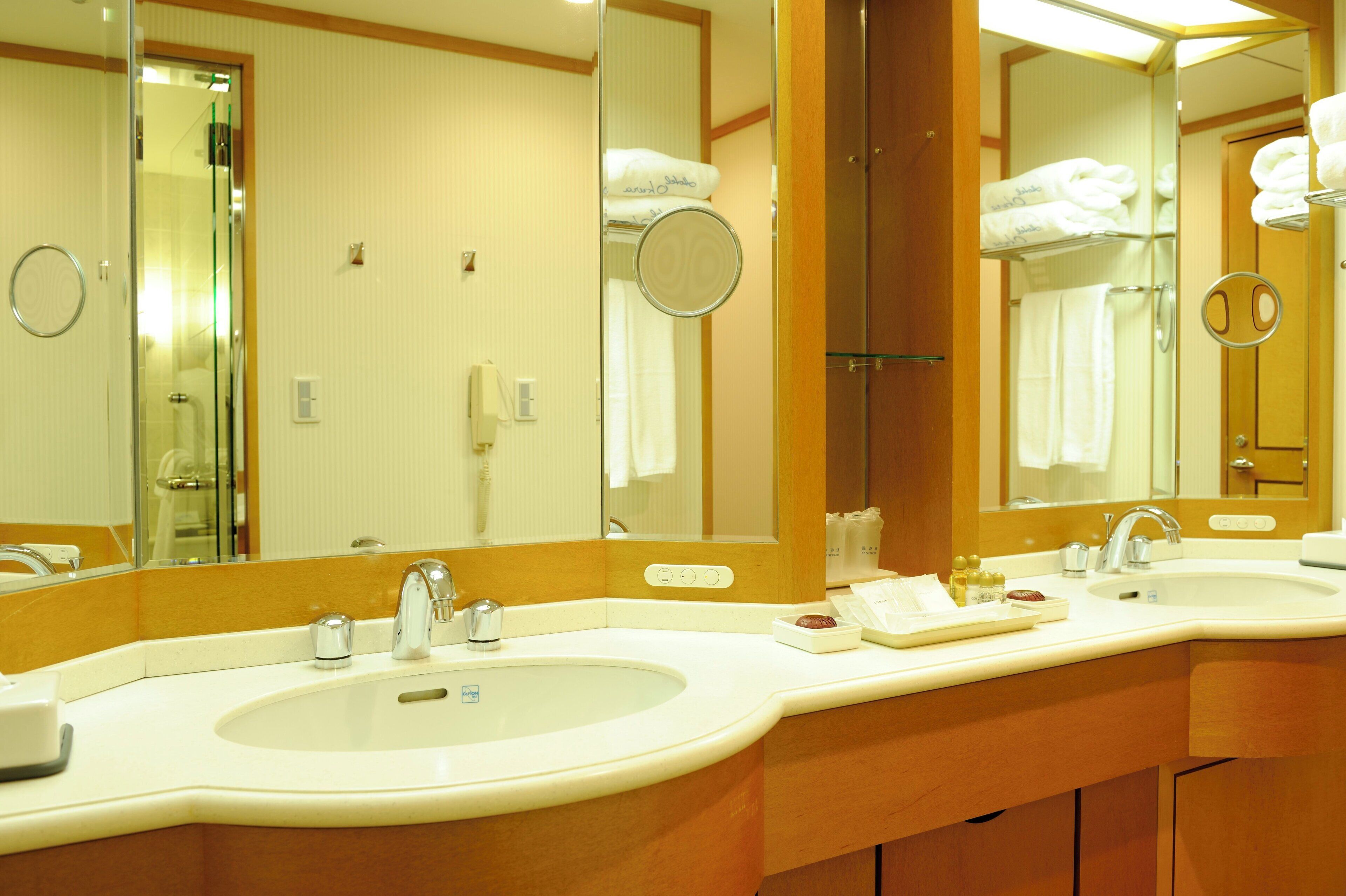 A hotel bathroom with two sinks, a large mirror, and towels on a rack.