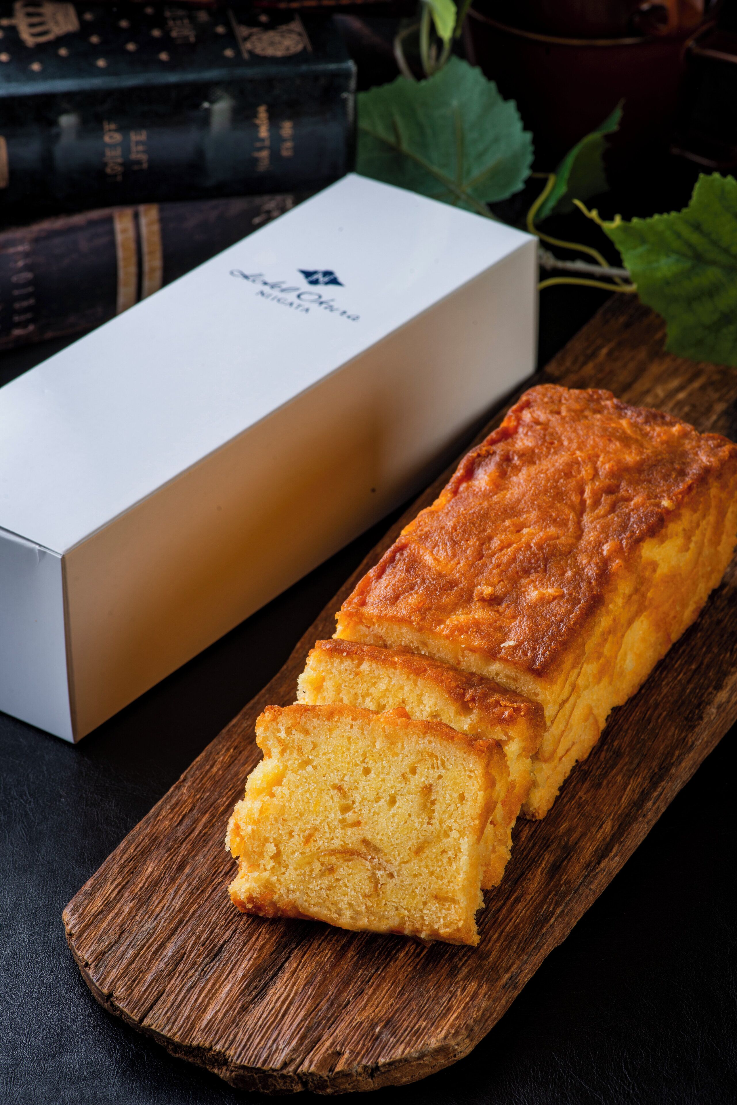 A loaf of bread on a wooden board with a white box in the background.