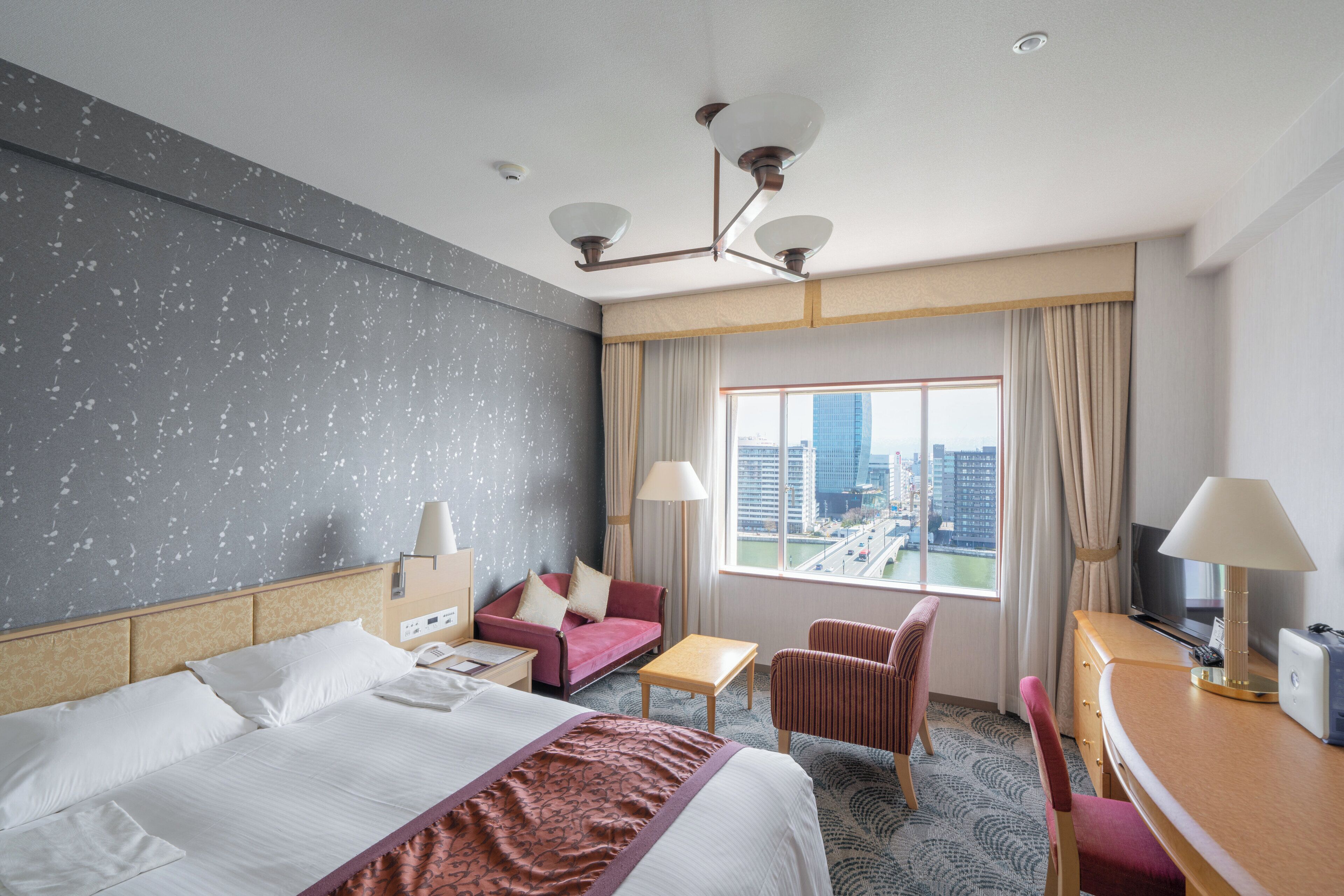 Ein Hotelzimmer mit einem großen Bett, einem Schreibtisch, einem Sessel, einer Couch und einem Fernseher.