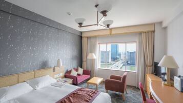 Ein Hotelzimmer mit einem großen Bett, einem Schreibtisch, einem Sessel, einer Couch und einem Fernseher.