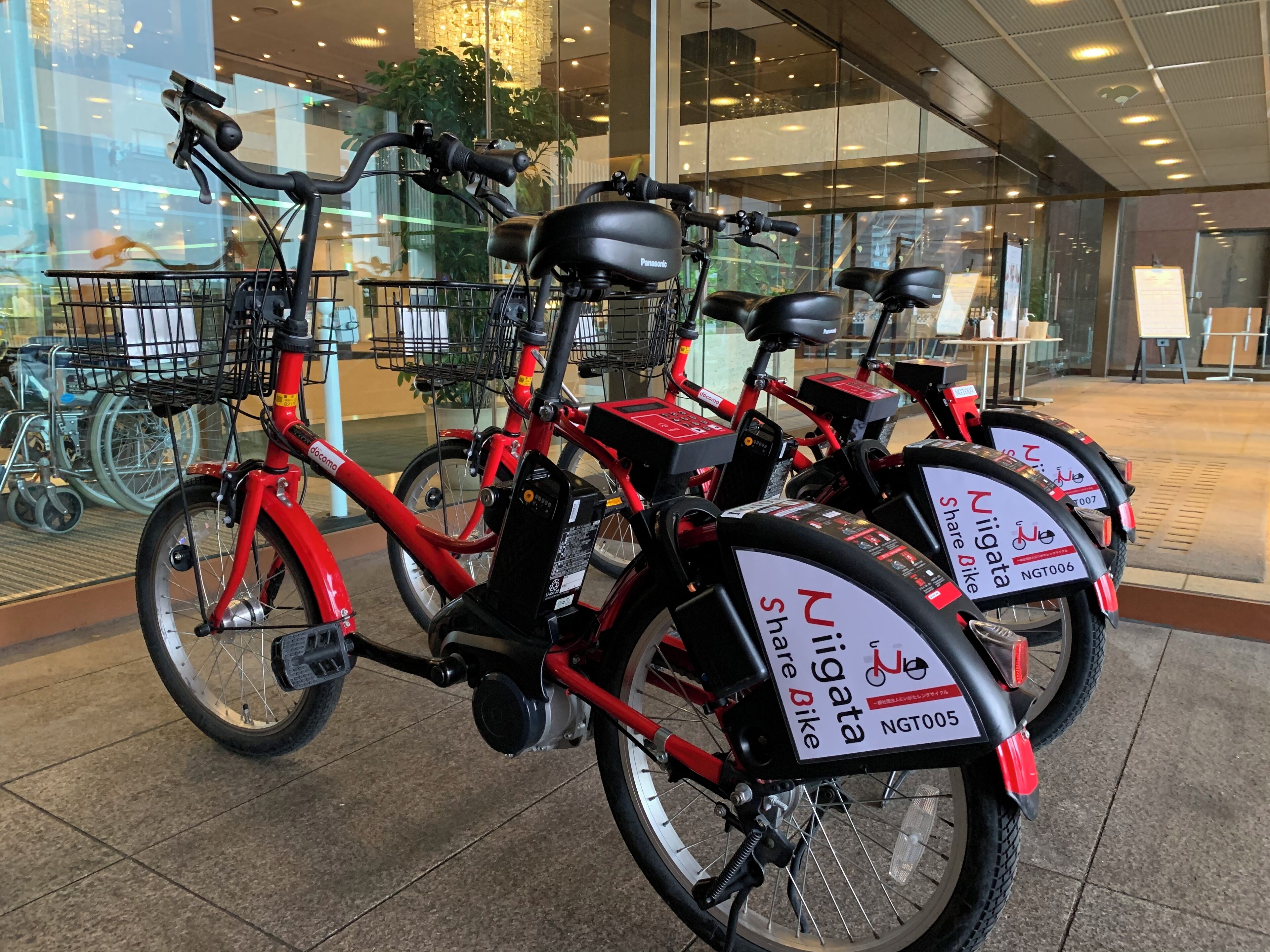 A row of red electric bikes with 'Niigata' branding, parked indoors with a modern interior and large windows.