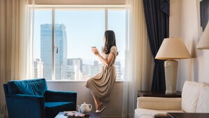 Una habitación con un ventanal grande, un sillón azul, un sofá blanco, una lámpara y un juego de té sobre una mesita.
