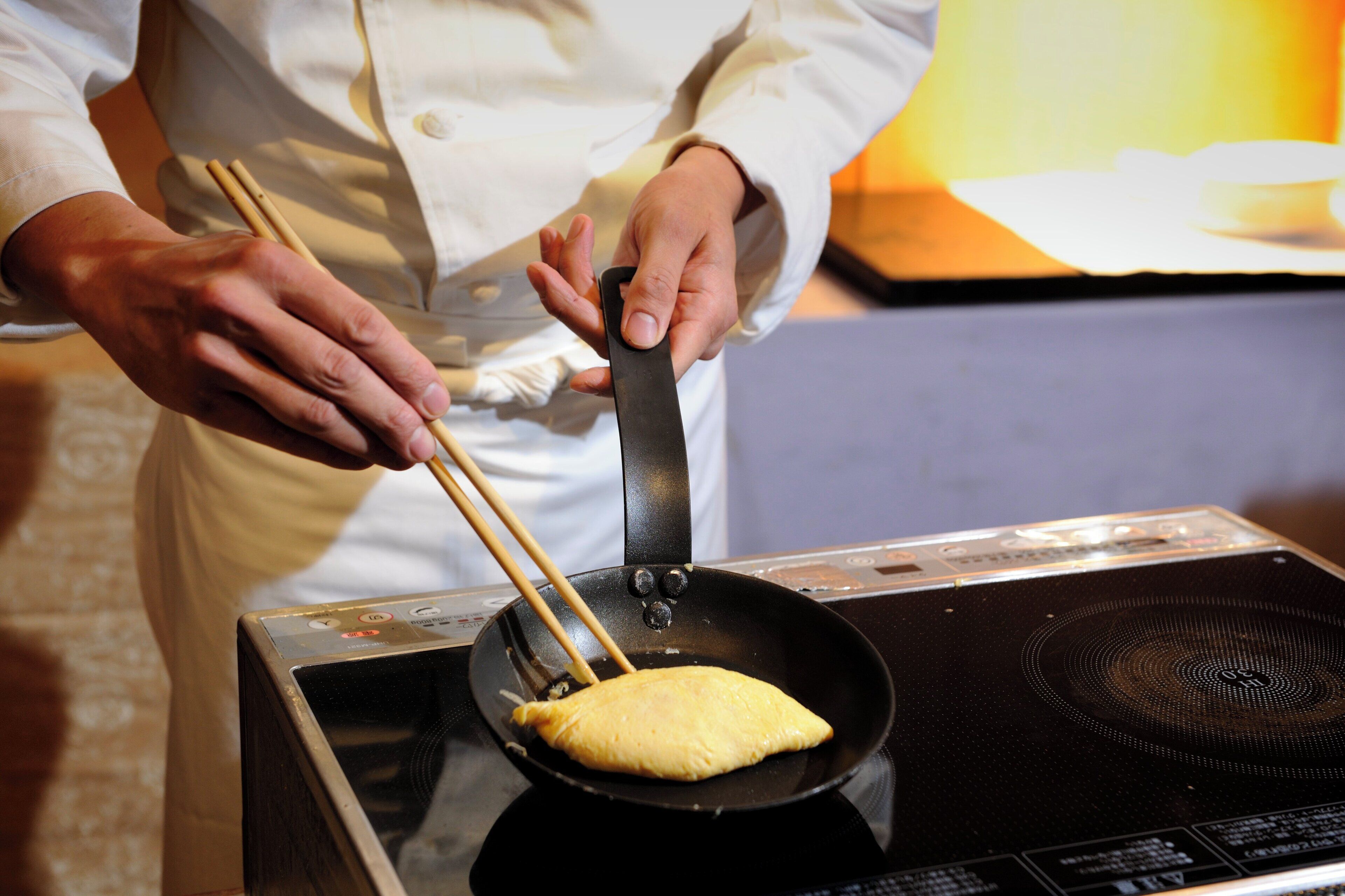 Una persona preparando una tortilla en una sartén antiadherente sobre una cocina por inducción.