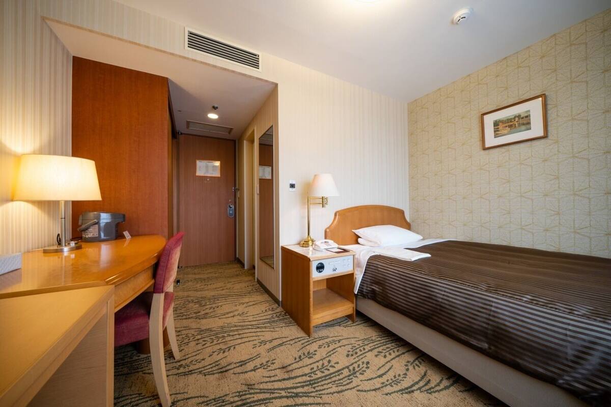 A hotel room with a bed, desk, chair, nightstand, and a wall-mounted picture.