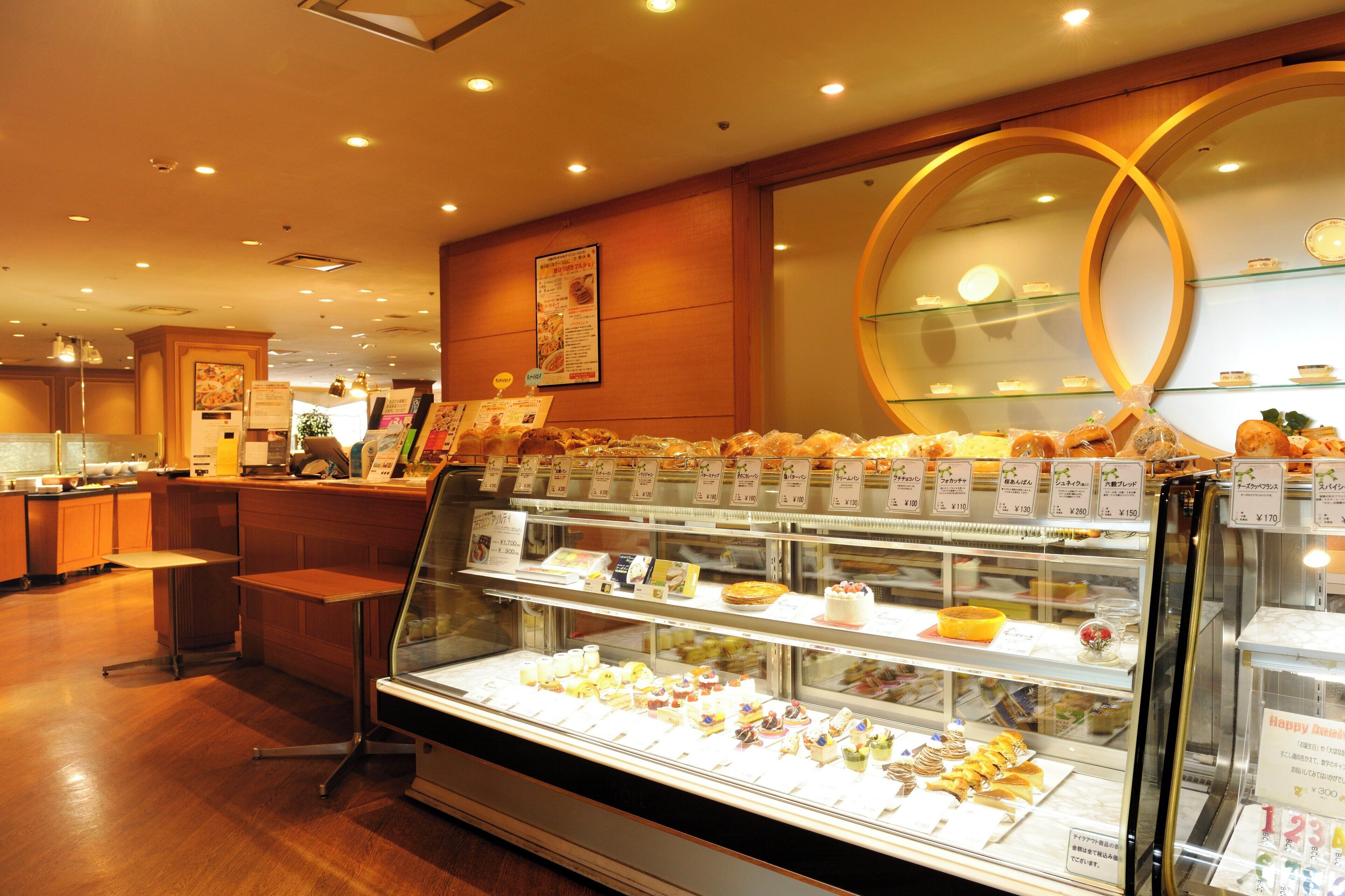 A bakery display case with various pastries and desserts, a wooden counter, and a menu board in a cafe setting.
