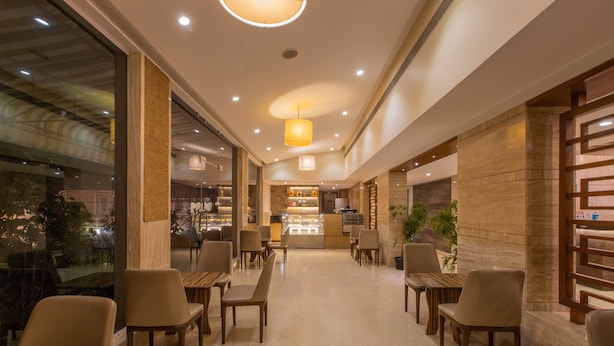 A modern hotel lobby with a central seating area, a kitchen in the background, and large windows on one side. - Nanutel Margao (Margao)