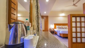 A hotel room with a bed, a nightstand, a lamp, a wooden partition, and a tray with a kettle, cups, and a bottle. - Nanutel Margao (Margao)