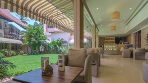 A hotel lobby with a central seating area, a reception desk, and a view of the outdoor garden. - Nanutel Margao (Margao)