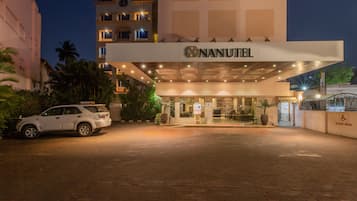 Entrada de un hotel con un coche blanco estacionado frente a él, un cartel que dice "NANUTEL" y un letrero de estacionamiento reservado.
