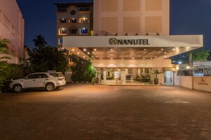 Entrada de un hotel con un coche blanco estacionado frente a él, un cartel que dice "NANUTEL" y un letrero de estacionamiento reservado.