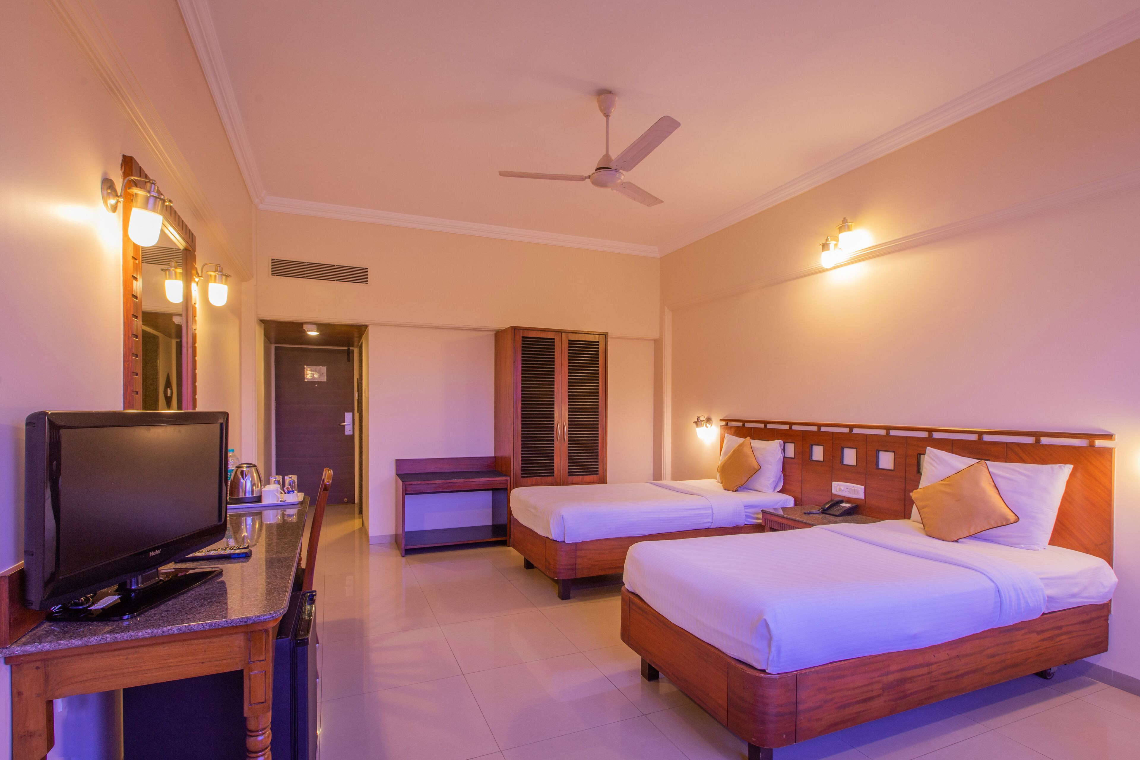A hotel room with two beds, a desk with a television, and a ceiling fan.