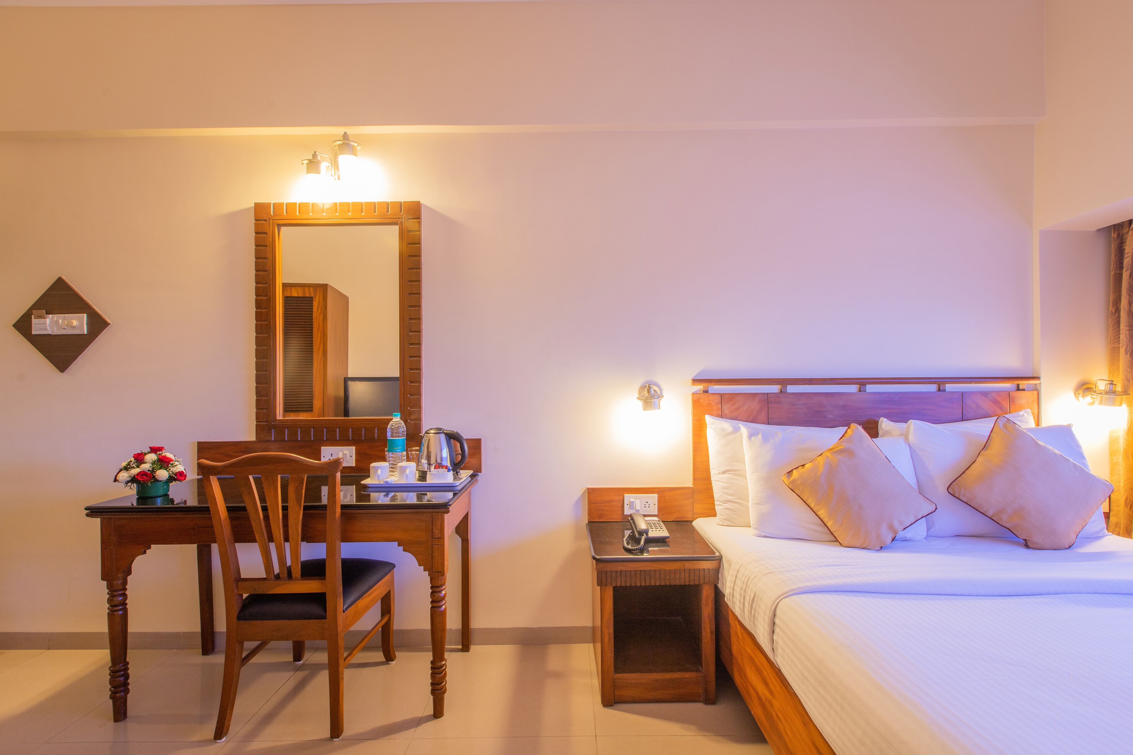 Una habitación de hotel con un escritorio de madera, una silla, una mesita de noche con un teléfono y una cama con almohadas.