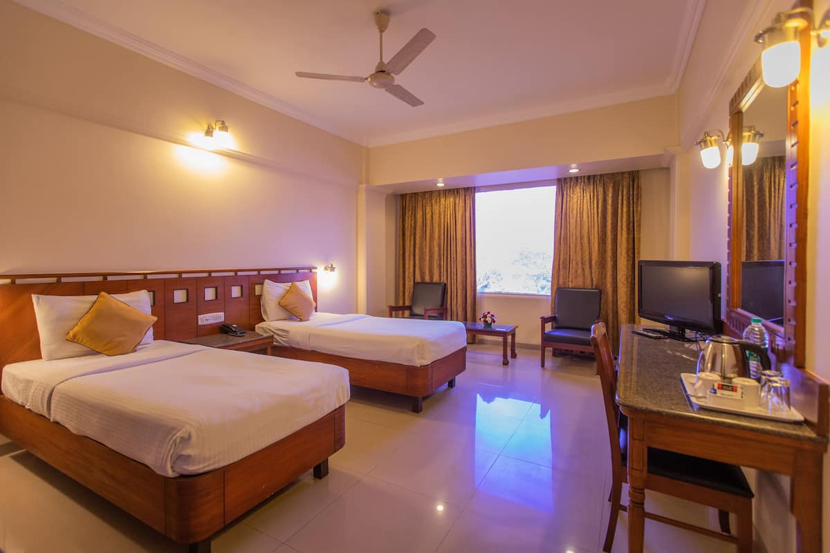 A hotel room with two beds, a desk with a chair, a television, and a ceiling fan.