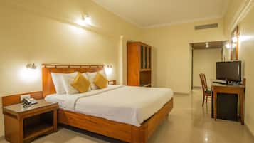 Habitación de hotel con cama de madera, mesita de noche con teléfono, escritorio con televisor y armario.