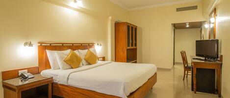 A hotel room with a wooden bed, bedside table with a phone, a desk with a TV, and a wardrobe.