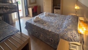 Quarto de hotel com cama, escrivaninha, cadeira, guarda-roupa e mesa de cabeceira com abajur e telefone.