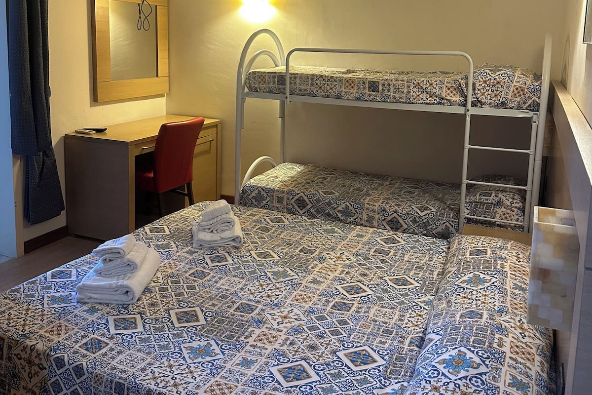 A room with a bunk bed, a desk, a chair, a television, and a wall-mounted light fixture.