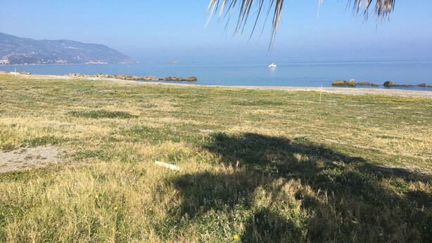 Paisagem costeira com céu claro, uma praia e um barco ao longe na água.