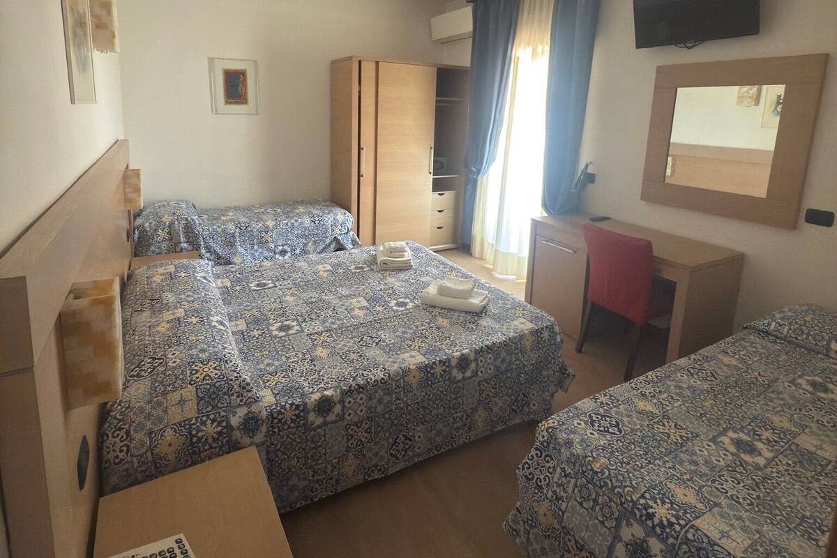 A hotel room with two beds, a desk, a chair, a TV, and a telephone.