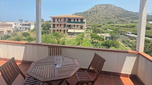 Uma área de estar coberta ao ar livre, com mesa e cadeiras, com vista para uma área residencial e uma colina.