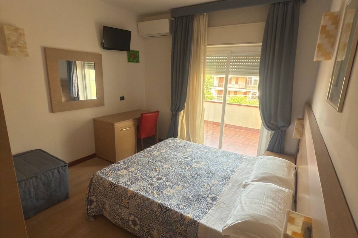 A hotel room with a bed, a desk, a chair, a TV, and a window with curtains.