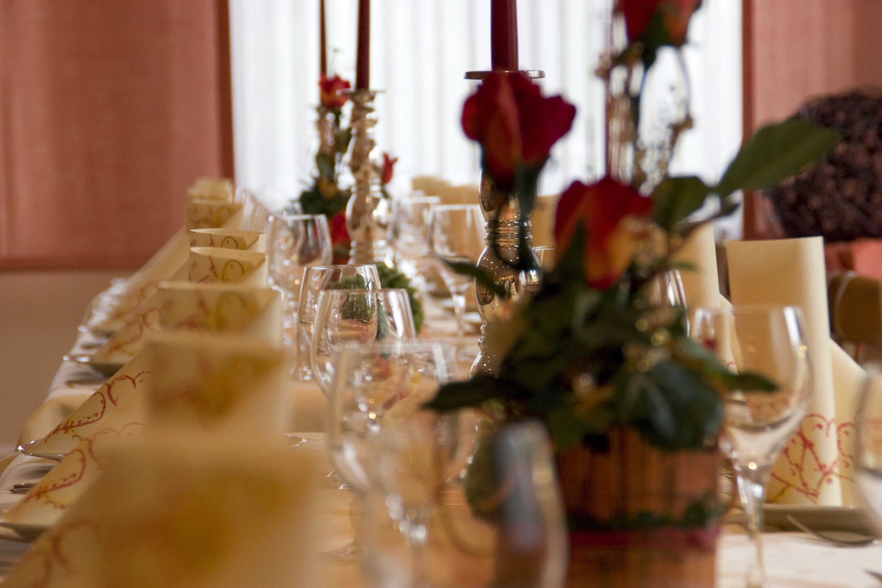 Mesa dispuesta para una ocasión formal con cristalería transparente, servilletas dobladas y un centro de mesa con una rosa roja.
