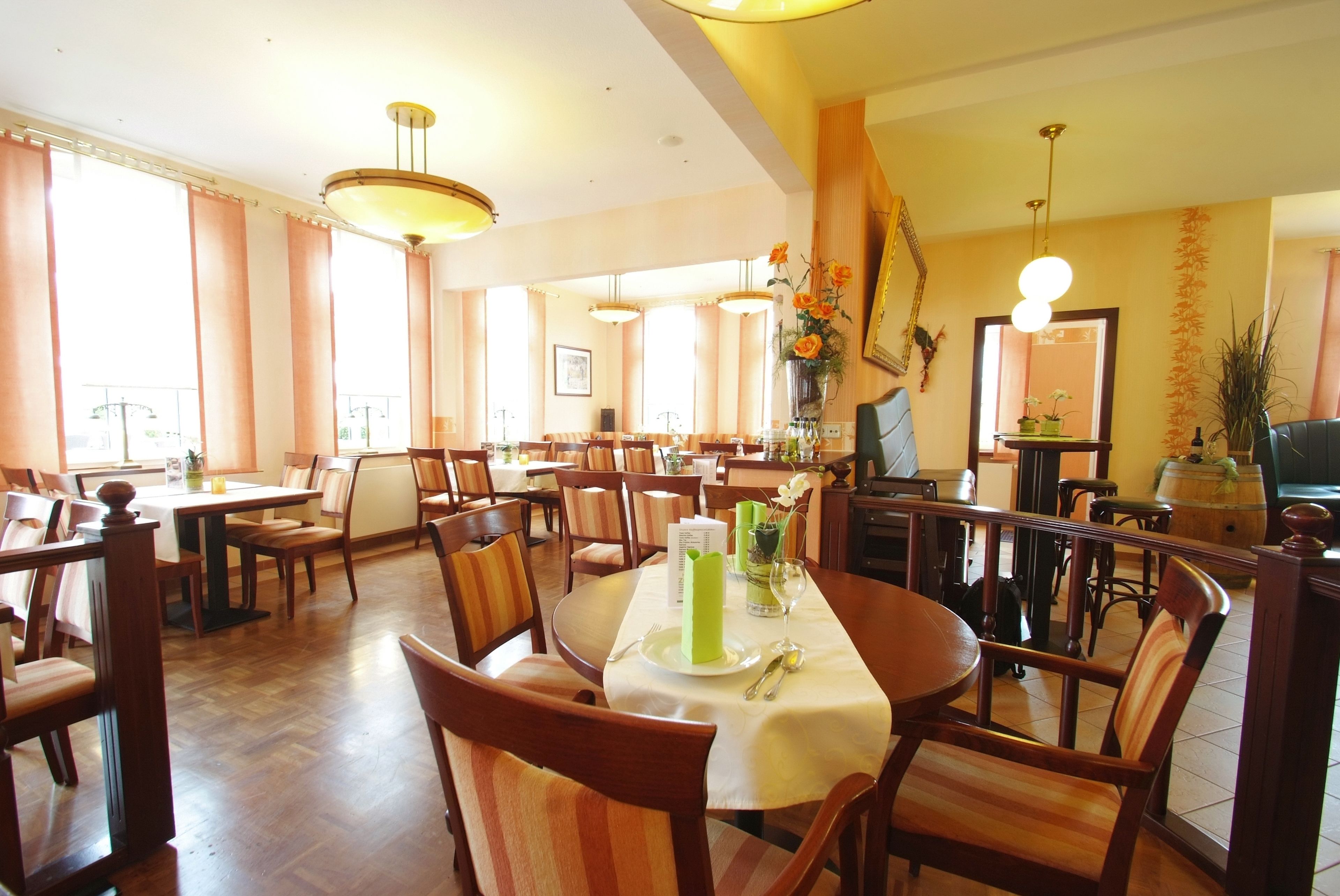 Een restaurant met houten tafels en stoelen, een groene decoratie in het midden en grote ramen.