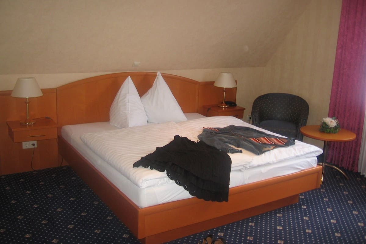 Une chambre d’hôtel avec un lit en bois, deux lampes de chevet, une chaise et une petite table agrémentée d’une fleur.