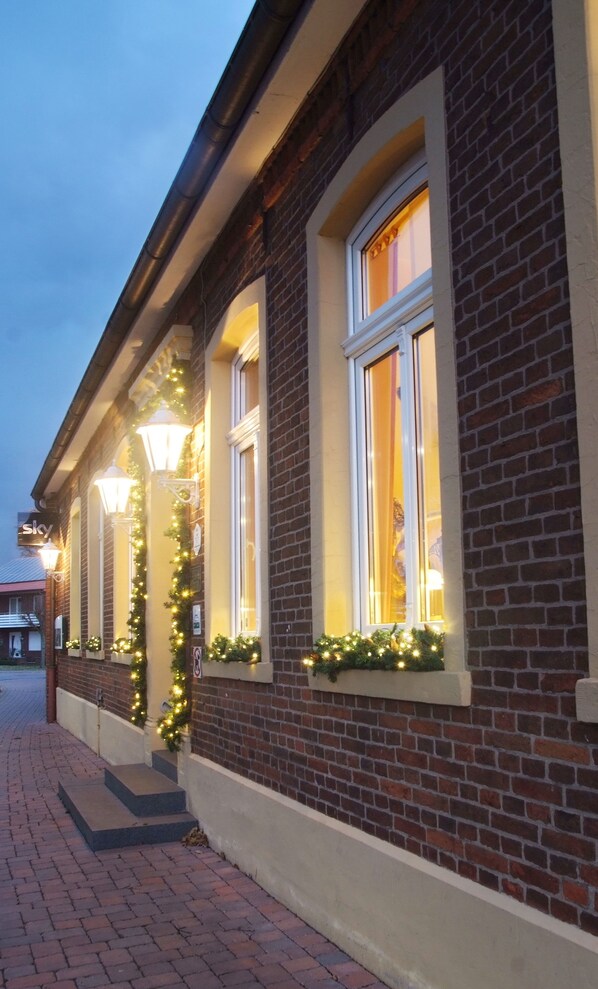 A brick building with three windows, each adorned with Christmas lights and garlands.