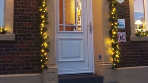 Entrada de un edificio con puerta blanca, paredes de ladrillo y luces decorativas.