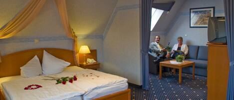 A hotel room with a bed, a sitting area, and a television.