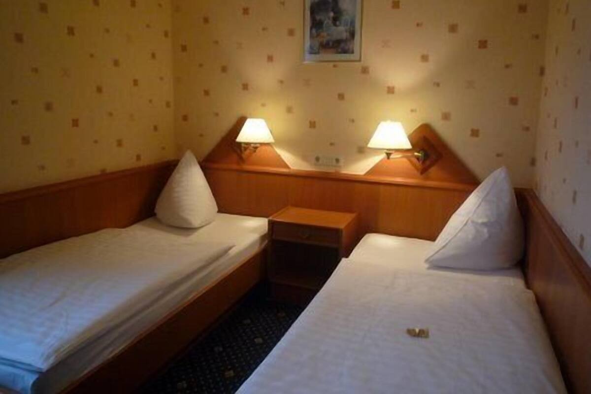 Une chambre d’hôtel avec deux lits simples, chacun étant équipé d’un oreiller et d’une table de chevet avec une lampe.
