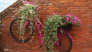A pink bicycle with baskets containing plants against a brick wall.