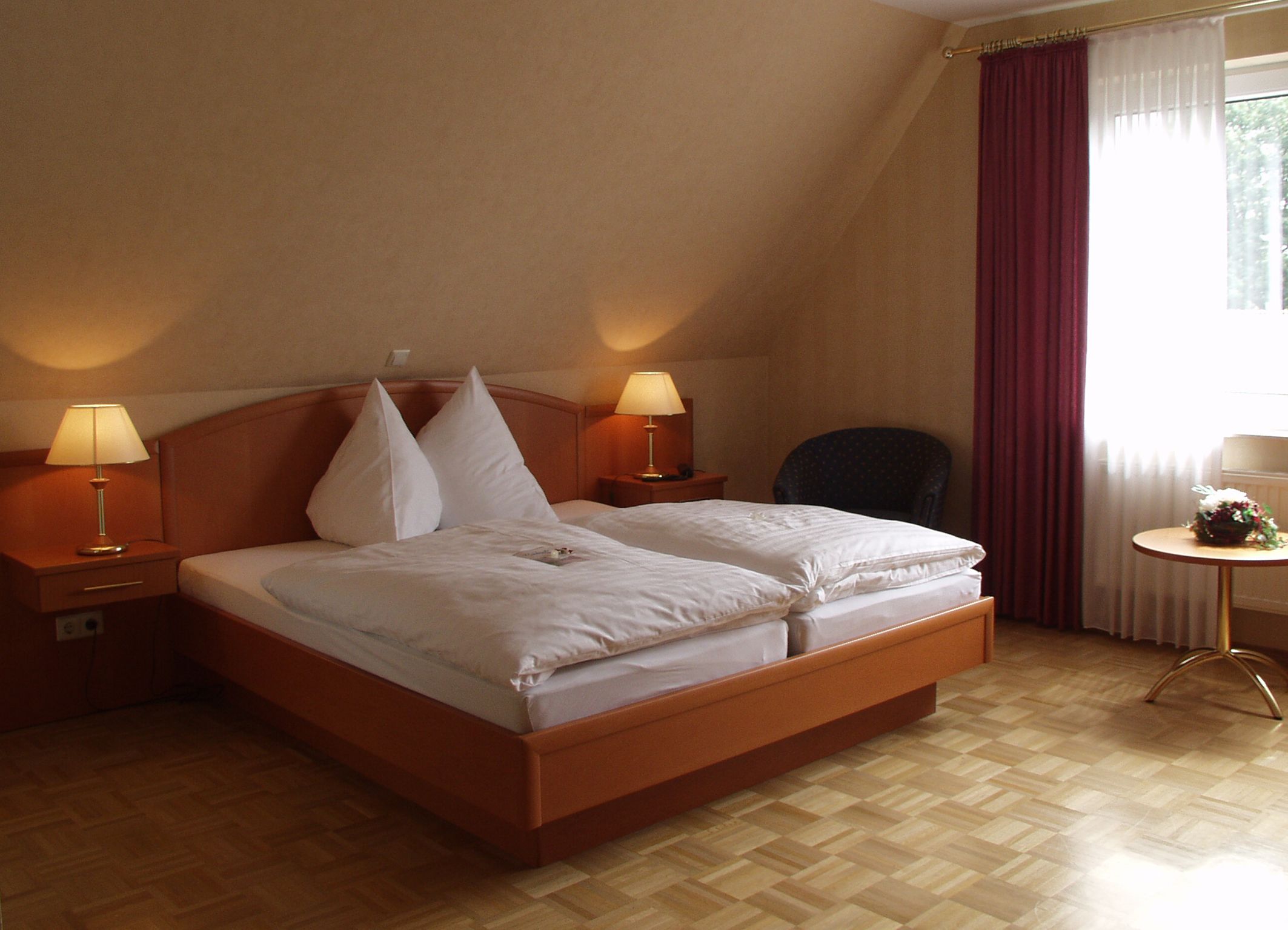 Ein Hotelzimmer mit einem hölzernen Bett, zwei Nachttischlampen, einem Sessel und einem kleinen Tisch mit Blumen.