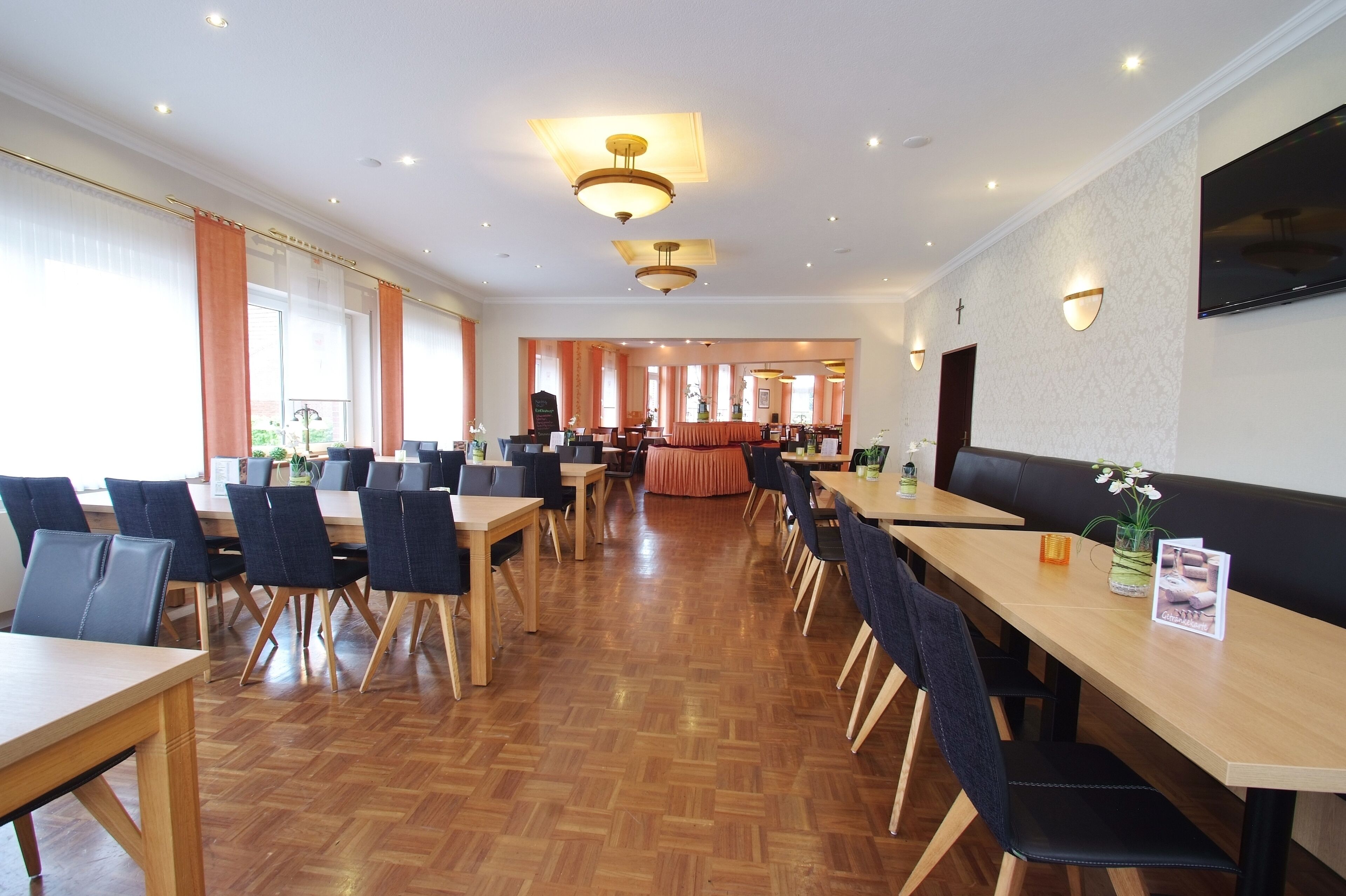 A spacious dining area with multiple tables and chairs, a wooden floor, and a television mounted on the wall.