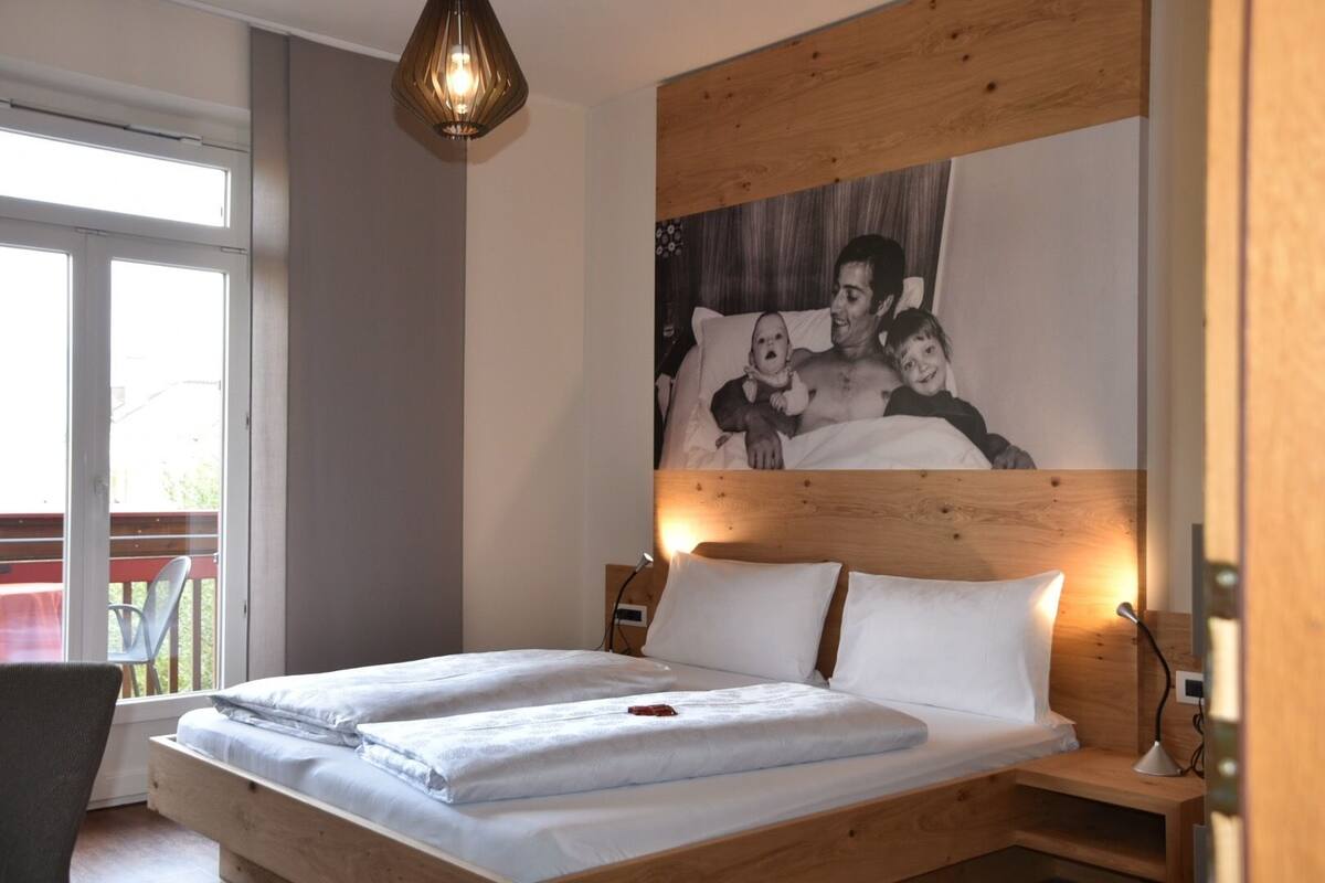 Une chambre à coucher avec une tête de lit en bois, un lit recouvert de draps blancs, une table de chevet et un tableau accroché au mur.