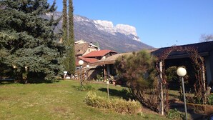 Un paysage montagneux, avec un ciel dégagé, un grand arbre à feuilles persistantes et un bâtiment doté d’un toit rouge.
