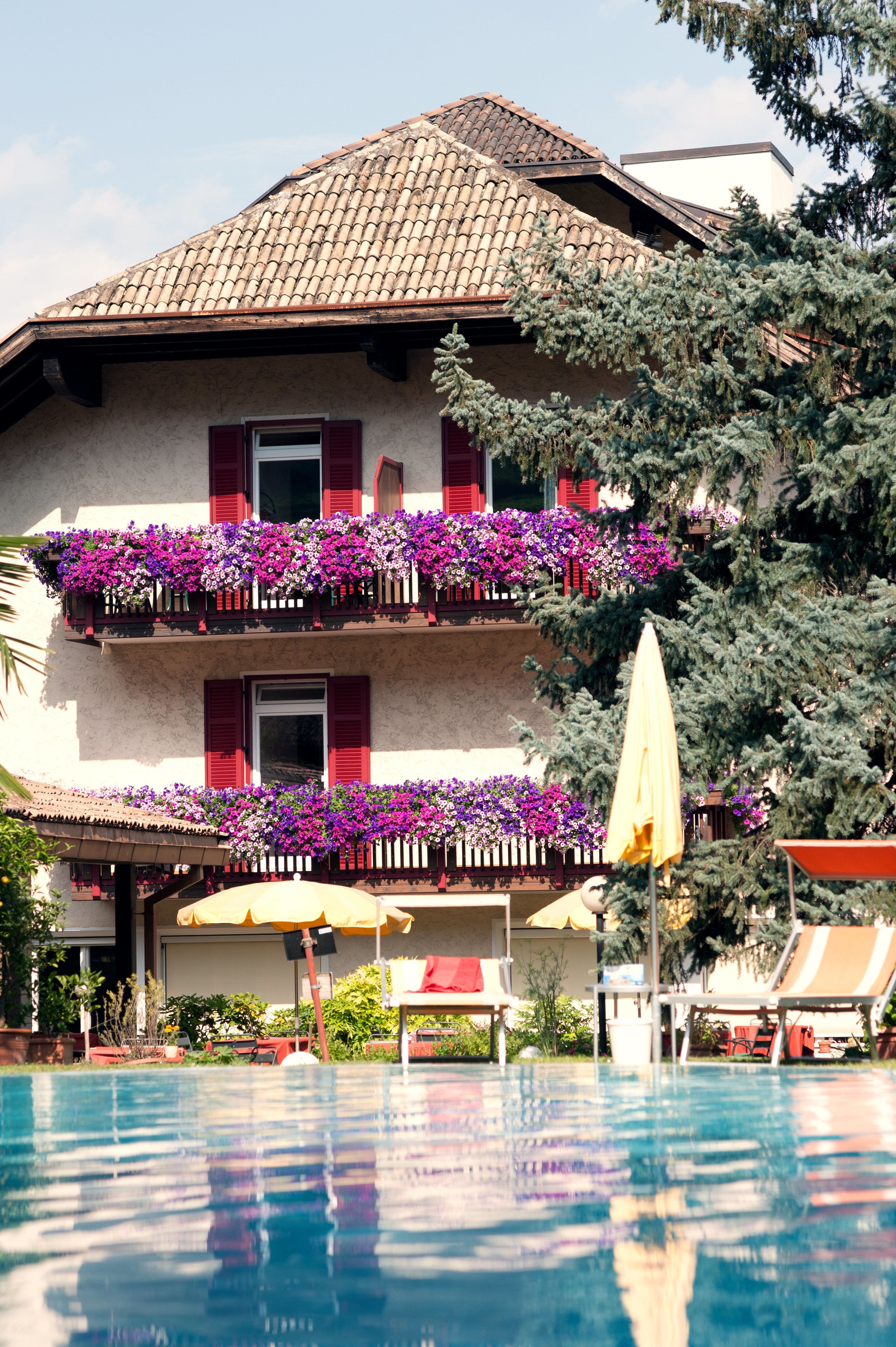 Ein Hotel mit Pool, roten Fensterläden und Blumenkästen an den Balkonen.