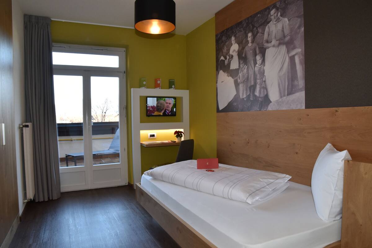 Une chambre à coucher avec un lit, une télévision, un bureau et une fenêtre avec des rideaux.