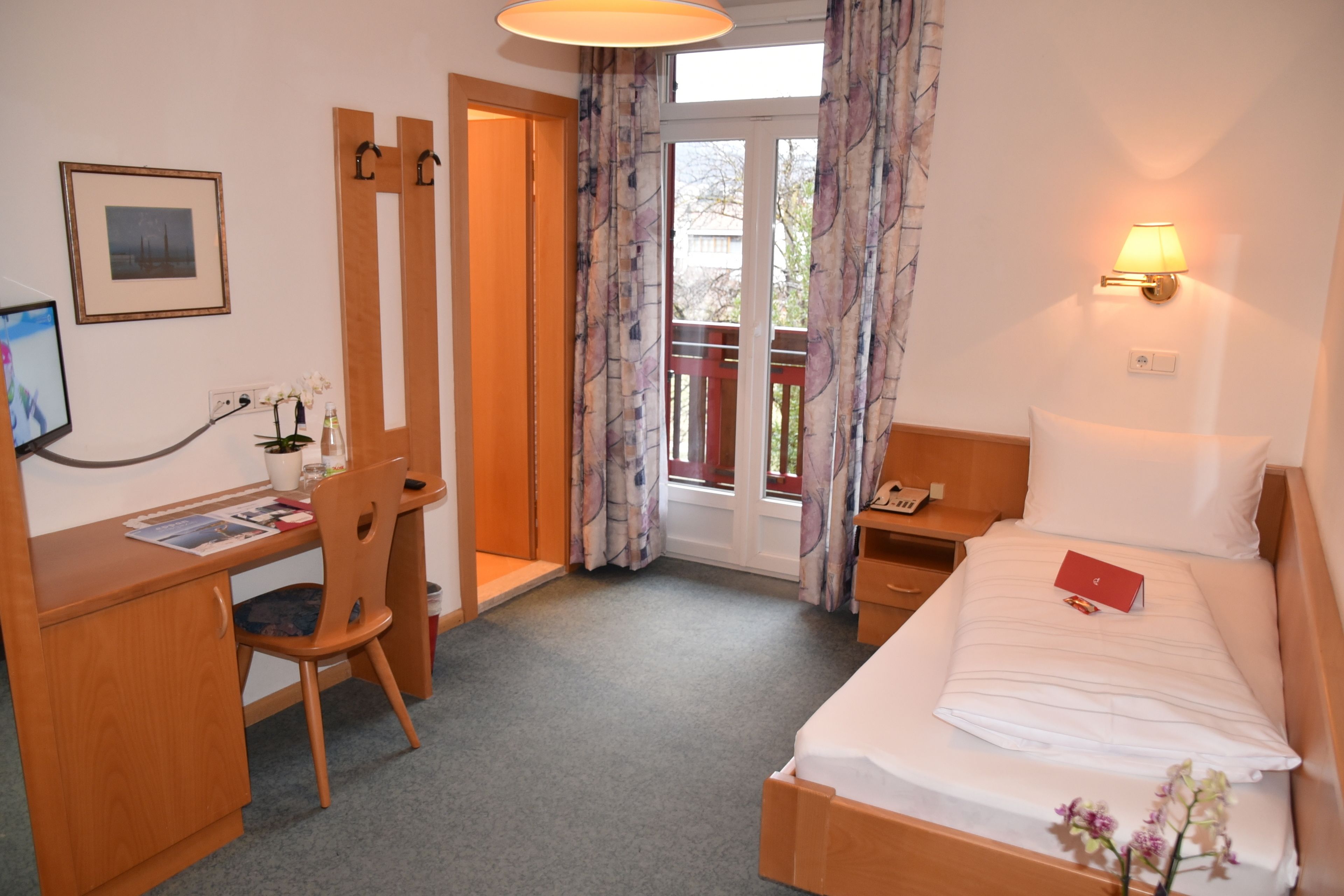 Een hotelkamer met een bed, bureau, stoel en een raam met gordijnen.