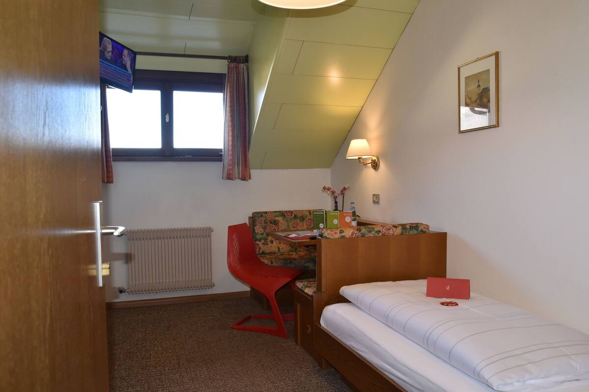 Une pièce comprenant un lit, un bureau avec une chaise, un radiateur, une fenêtre avec des rideaux et un tableau accroché au mur.