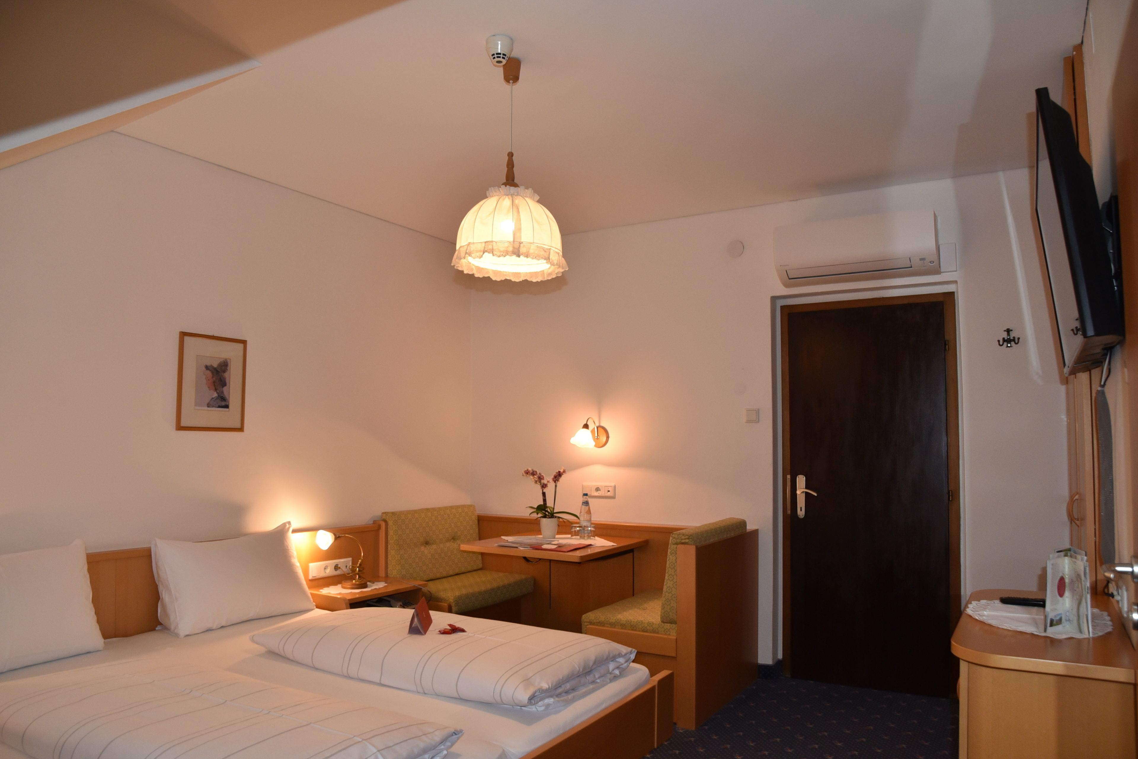 A hotel room with a bed, a desk, a chair, a TV, and a door.