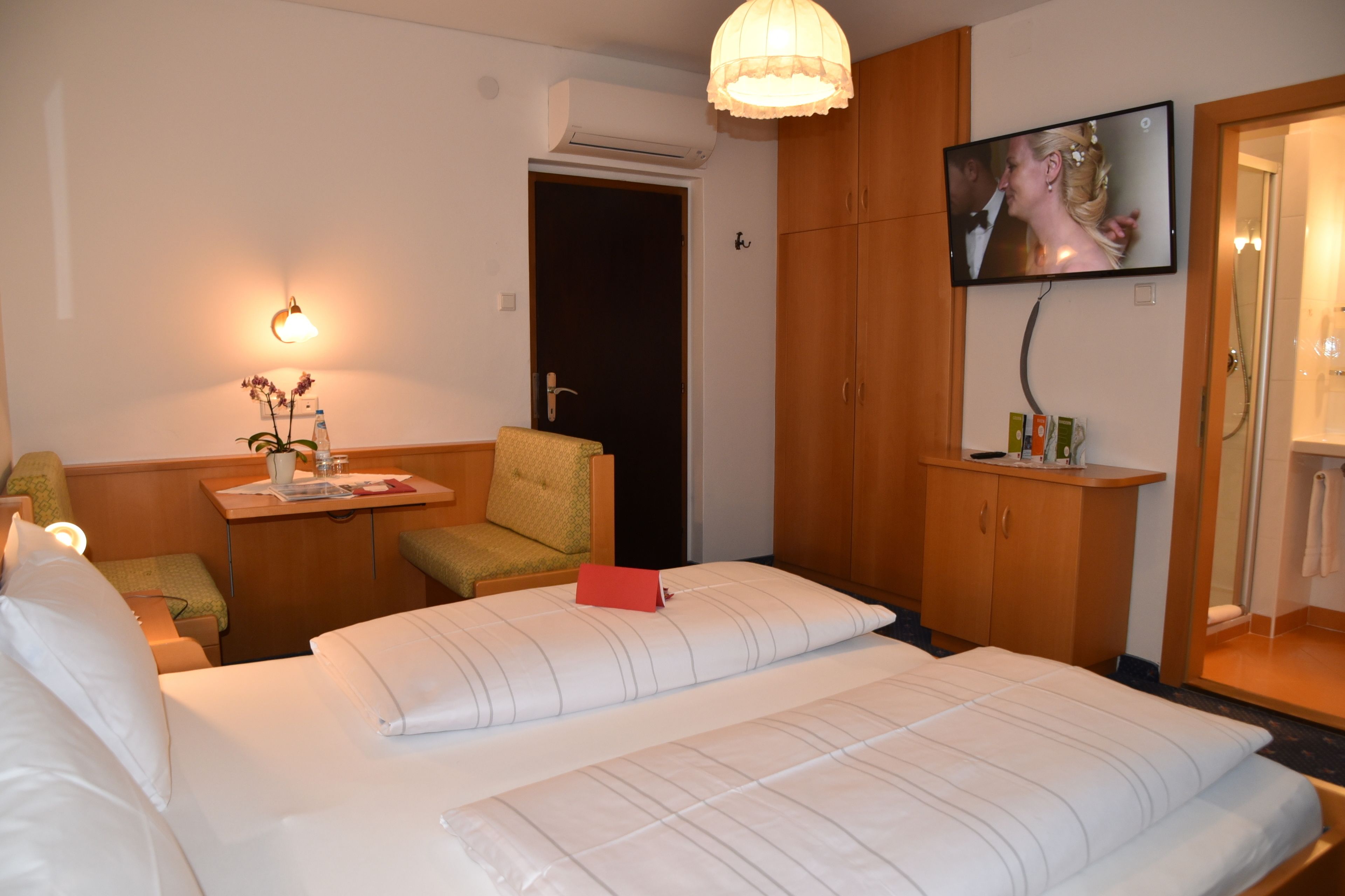 Una camera d'albergo con un letto, una TV a parete, una scrivania con una sedia e un armadio.