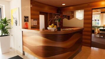 A reception desk with a wooden design, a potted plant, and a bowl of fruit.