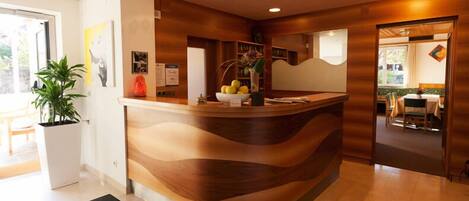 A reception desk with a wooden design, a potted plant, and a bowl of fruit.