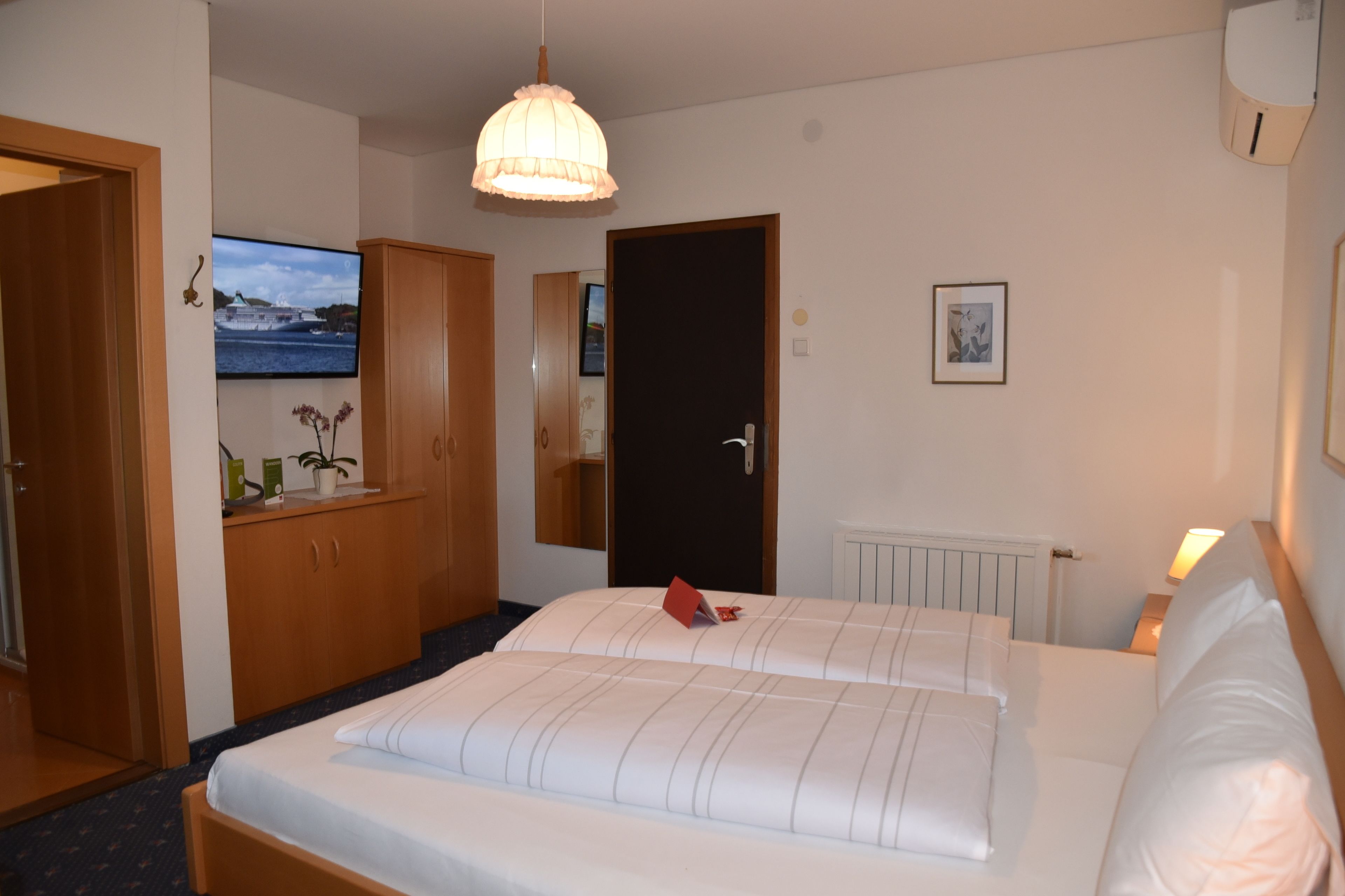 A hotel room with a bed, a television mounted on the wall, a wardrobe, and a door.